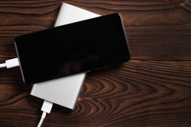 Powerbank and charge smartphone on wooden table.