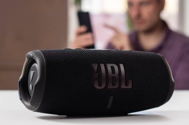 Dnioro Ukrayna. 27 Ocak 2023: Akıllı telefon tutan ve taşınabilir müzik hoparlörü kullanan adam JBL şarj 5.
