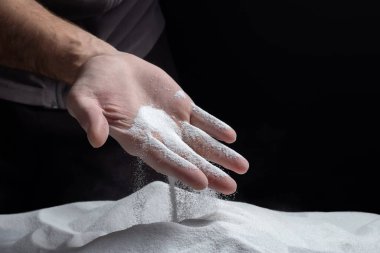 Siyah arka plandaki parmaklar aracılığıyla kum. Hayatın akışı kavramı..