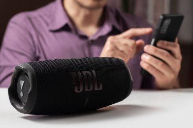 Dnioro Ukrayna. 27 Ocak 2023: Akıllı telefon tutan ve taşınabilir müzik hoparlörü kullanan adam JBL şarj 5.