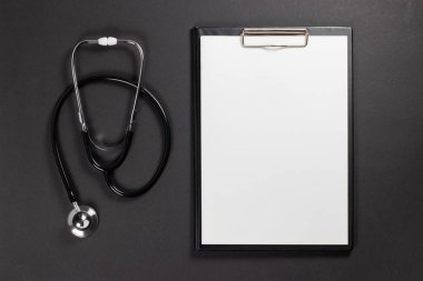 Üzerinde beyaz kağıt olan bir dosya ve steteskop, koyu bir arkaplan üzerine kurulmuş..