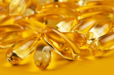 Sarı arka planda üç kapsül Omega 3 ve bulanık arkaplanda da bir sürü kapsül. Sağlık hizmeti kavramı.