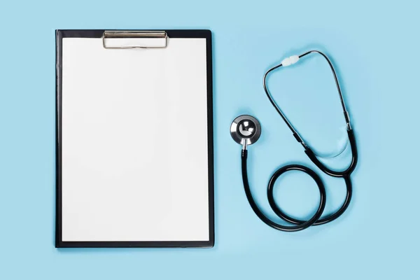 Blank clipboard with stethoscope on blue background.