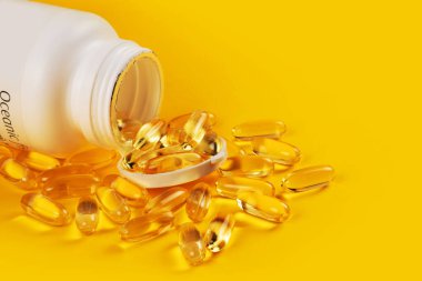 Omega 3 ve sarı zemin üzerinde D vitamini bulunan balık yağı kapsülleri.