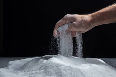 Siyah arka plandaki parmaklar aracılığıyla kum. Hayatın akışı kavramı..