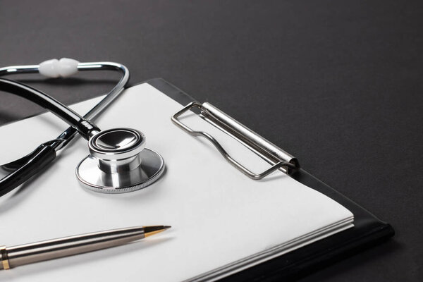 A clipboard and stethoscope with white paper on it, set against a dark background.