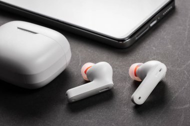 Kablosuz beyaz kulaklık, siyah arka planda çanta ve akıllı telefon..