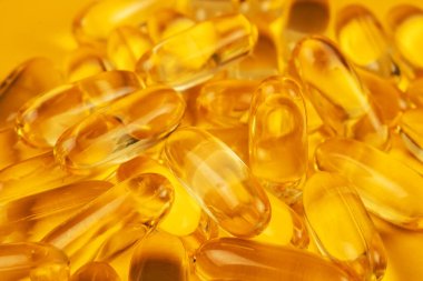 Omega 3 ve sarı zemin üzerinde D vitamini bulunan balık yağı kapsülleri.