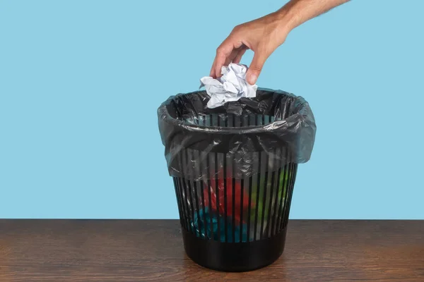 Hand throwing out paper into a trash basket.