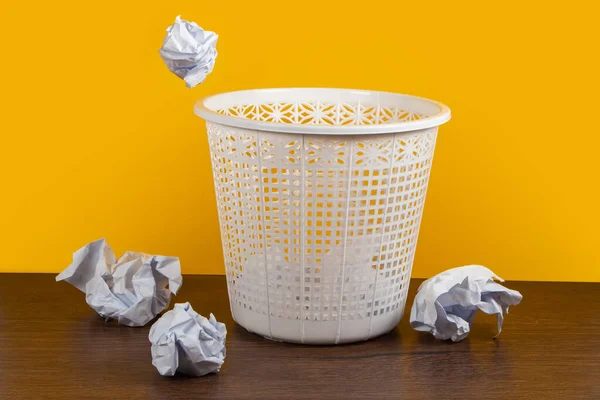 Crumpled paper in the trash can on yellow background.