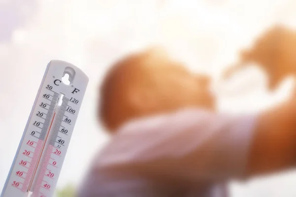 Aşırı sıcakta su içen adam, yaz gününde termometre, arka planda güneş olan yüksek sıcaklığı gösterir veya gösterir..