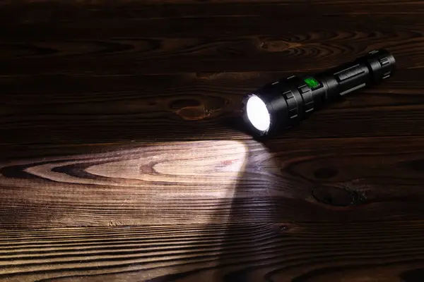 Flashlight and a beam of light in darkness. A modern led lamp with bright projection on dark wood table. Surface with copy space.
