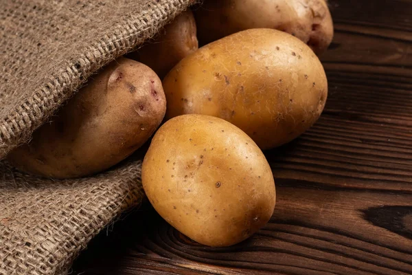 Raw potato food. Fresh potatoes in an old sack on wooden background.
