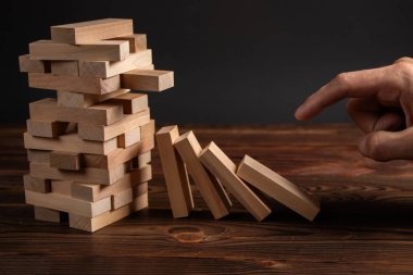 Finansal risk yönetimi ve stratejik planlama dominosu kavramları olan tahta bir Jenga bloğunu iten parmaklar.