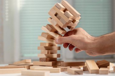İş adamı, tahta bloğu düşen kuleden kaldırıyor. Tahta jenga oyunuyla risklerin yönetimi ve ekonomik istikrarsızlık kavramı. Şirket işinde başarısızlık ve çöküş