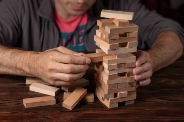 Koyu kahverengi masada Jenga oyunu için ahşap bloklar yığan erkek elleri, karantina sırasında evde kalırken, aile aktiviteleri, parti panosu oyun konsepti devre dışı