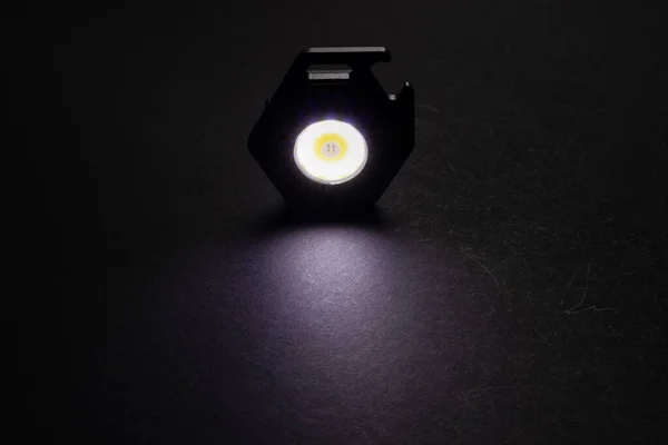 LED Flashlight Keychain and a beam of light in darkness. A modern led lamp with bright projection on dark table