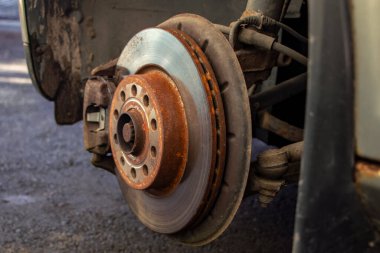 Arabada kalibre ve fren pedleri olan eski bir ön fren diski, bir atölyede araba kaldırma, fren kalibreli yakın plan.