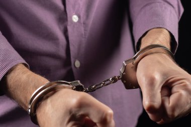 Sandalyede kelepçeli bir adam var. Elleri kelepçeli adamlar suçtan tutuklandı. Elleri arkada, çocuk cezaevi şiddet konseptinde prangalı..
