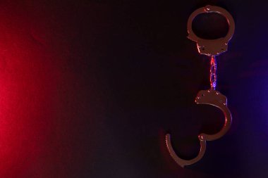 Gece polis baskını ve sen tutuklusun. Kelepçelerin silueti. Flaşlı kırmızı ve mavi polis ışıkları koyu arkaplan.