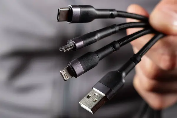 The hand holds a universal USB cable. USB Type C, Micro USB, Usb lightning.