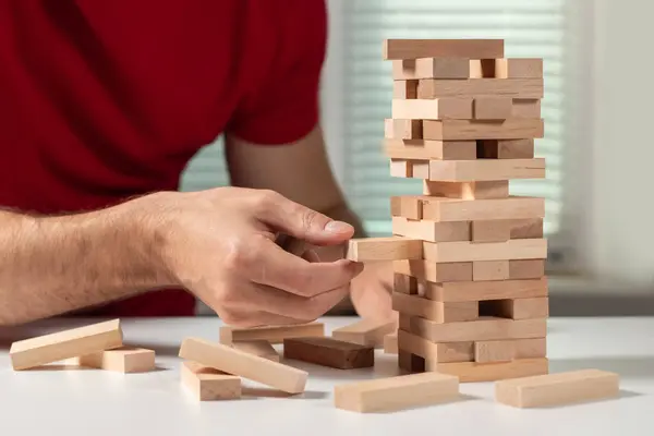 The tower from wooden blocks and man's hand take one block.