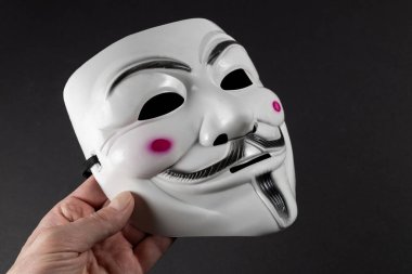 Dnipro. Ukraine 30 jan 2024: Vendetta mask in hand on dark background. This mask is a well-known symbol for the online hacktivist group Anonymous. clipart
