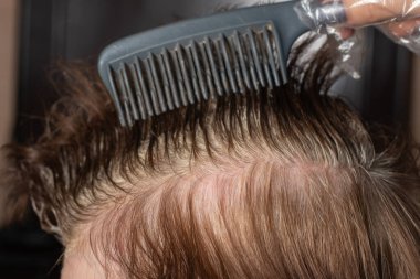 Yakından bir kadın saçını siyah bir fırçayla boyuyor. Evde beyaz saç boyası