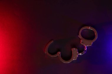 Gece polis baskını ve sen tutuklusun. Kelepçelerin silueti. Flaşlı kırmızı ve mavi polis ışıkları koyu arkaplan.