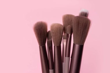 Pembe arka planda çeşitli makyaj fırçaları.