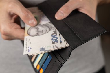 500 hryvniadan oluşan banknot erkek elinde. Üzerinde Ukrayna parası ve kredi kartları olan gri cüzdan..