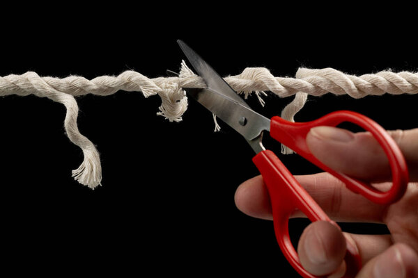 Worn rope ready to break, with scissors on black background