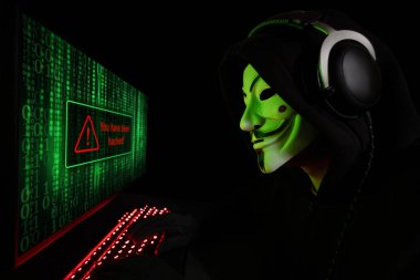 Dinyeper. Ukrayna. 03 Şubat 2024: beyaz maskeli ve kapüşonlu isimsiz bilgisayar korsanı. Siber saldırı için bilgisayar kullanan karanlık yüz, veri hırsızı, internet saldırısı, darknet ve siber güvenlik kavramı.
