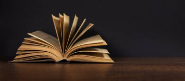 Tahta bir masanın üzerinde duran açık eski bir kitap. Koyu arkaplan.