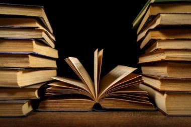 Açılmış kitap ve eski kütüphanedeki ahşap masanın üzerindeki eski kitap yığınları. Tarihi kitaplar arka planında. Retro tarzı. Tarih ve eğitim hakkında kavramsal geçmiş
