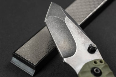 Adam, karanlık bir masada bileme taşı kullanarak bıçağı keskinleştiriyor..