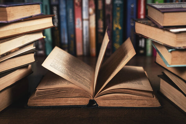 Education learning concept with opening book or textbook in old library, stack piles of literature text academic archive on reading desk and aisle of bookshelves in school study class room background.