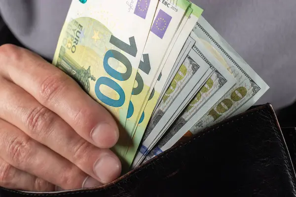 Man handing wallet with 100 euro and 100 dollars banknotes.