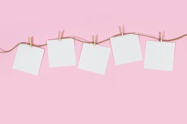 Pembe arka planda elbise askıları üzerine beyaz kağıt kartlar.
