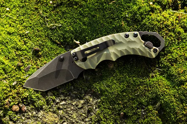 Tactical folding knife for survival on moss background.
