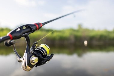 Sahilde suyun yanında dönen çubuk, çelik kırmızı makaraya yakın çekim. Balıkçılık hobisi, spor ve eğlence konsepti.