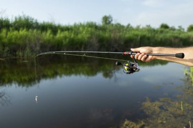Yazın taze su balıkçılığı. Dönen bobin, bir balıkçının elinde dönen bir çubuk..