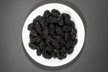 Siyah arka planda beyaz tabakta taze siyah dut. Sulu ve sağlıklı mevsimlik bahçe meyveleri kavramı.