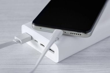 Powerbank ve akıllı telefonu beyaz ahşap masada şarj et.