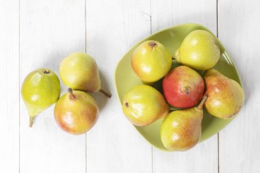 Beyaz ahşap zemin üzerinde seramik bir tabakta taze armutlar. en üstteki görünüm.