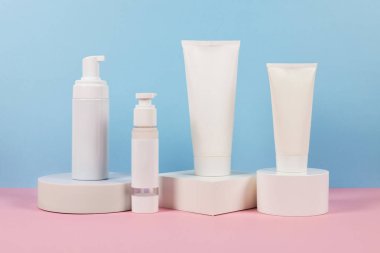 Cilt için kozmetik. Mavi ve pembe arka planda podyuma yerleştirilmiş farklı kozmetik konteynırlar. Dispanser ve tüpler. Cilt bakımı veya güzellik ürünleri.