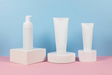 Reklamlar için güzel kozmetik şablonlar, plastik krem tüpleri ve podyumlu mavi arka planda şişeler. Premium ürün için güzellik tasarımı