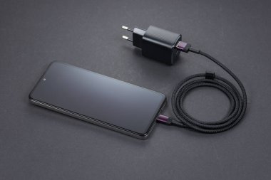 Koyu arkaplanda şarj aleti olan cep telefonu.