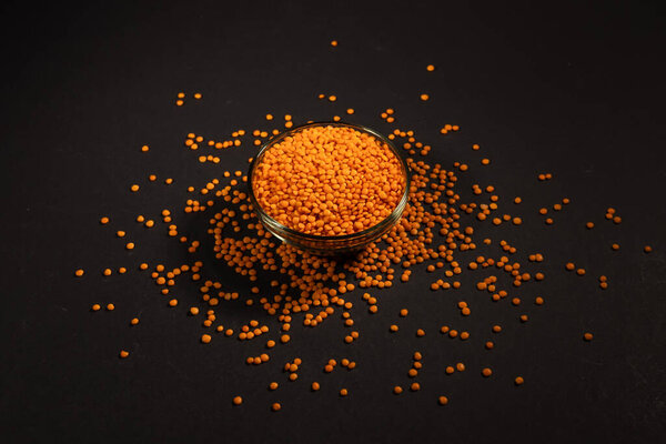 Красная чечевица в стеклянной миске. Сухие оранжевые чечевица зерна, куча даль, сырой даал, даль, мазур, линза culinaris или линзы esculenta на темном фоне