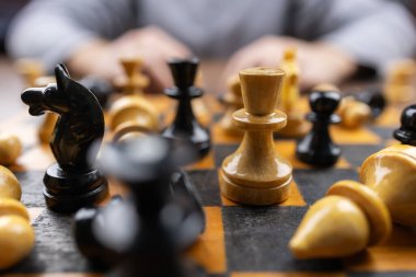 Masada otururken satranç tahtasının üzerindeki satranç taşını kapat. Oturma odasında abur cubur ve içeceklerle otururken arkadaşlarla strateji oyunu oynayan kişi.